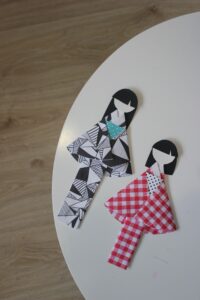 Na fotografii dwie papierowe lalki w kimonach, jedna w czarno-białym w geometryczny wzór, druga w czerwono-białą kratę. Wygląd lalek nawiązujący do kultury Japonii.